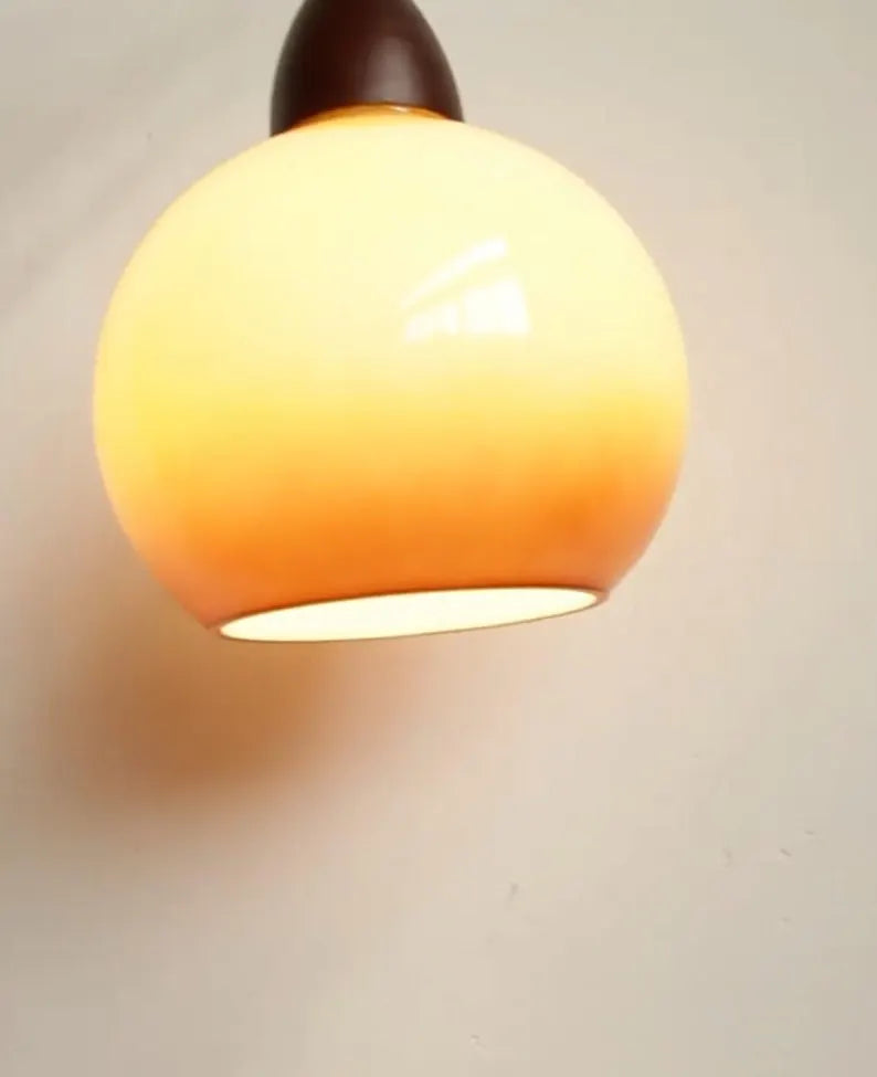 Lampada a sospensione in vetro sfumato color ambra accesa su parete chiara
