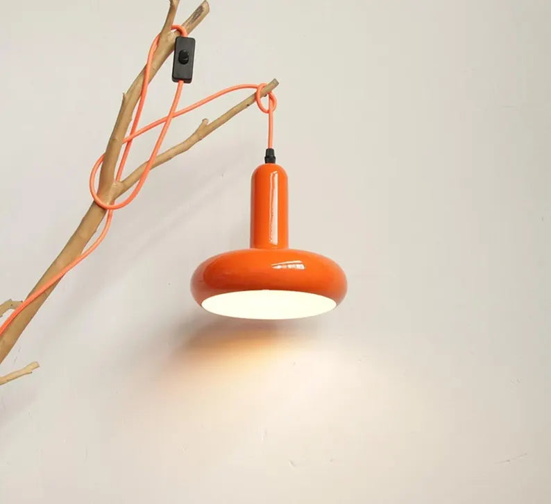 Lampada arancione accesa con luce calda sospesa a parete su sfondo chiaro