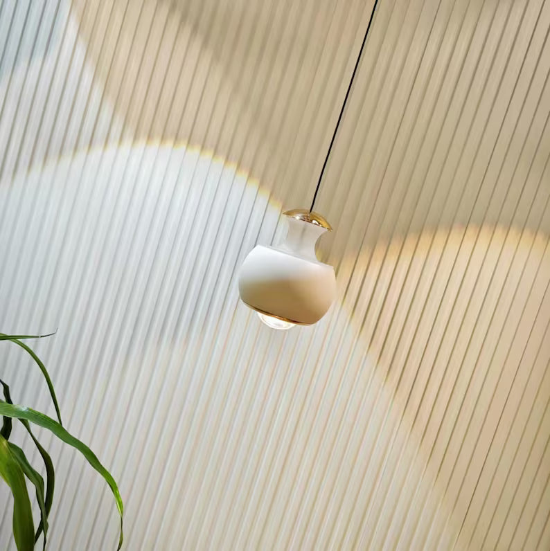 Lampada sospesa di design che diffonde luce calda su parete moderna